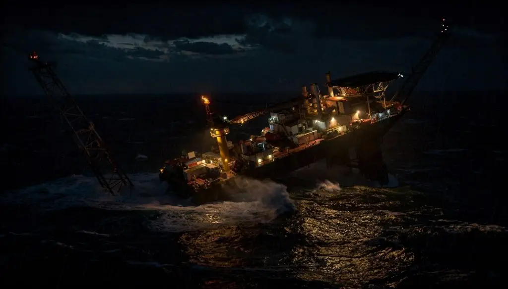 Offshore oil platform partially capsized at night in rough seas
